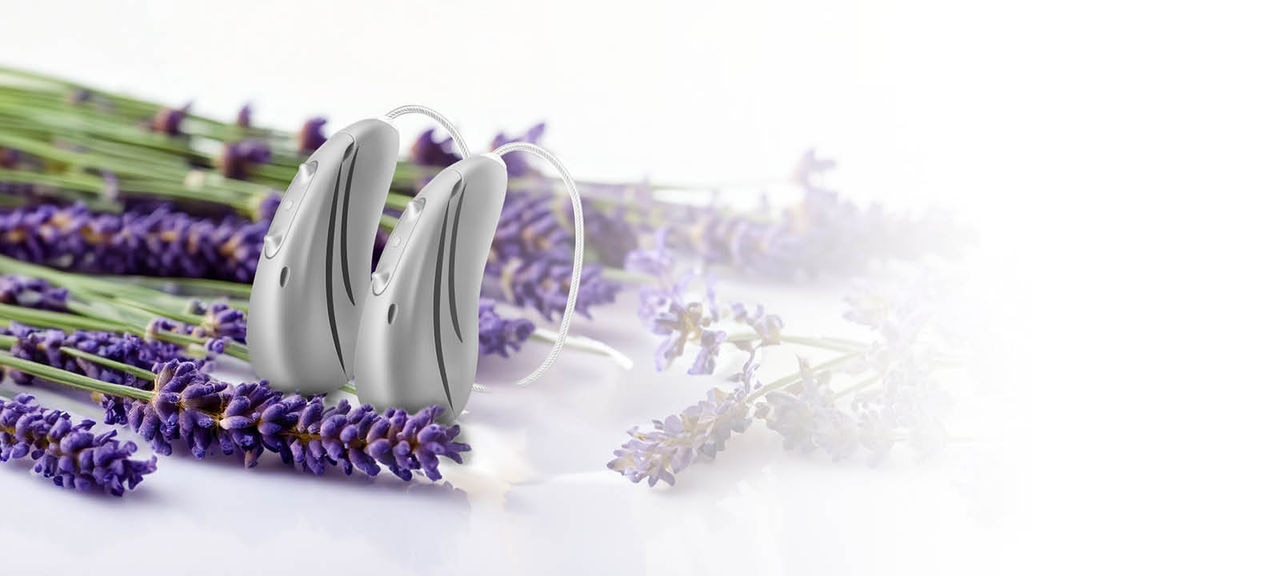 Pair of Hansaton sound E-R hearing aids next to lavender Pair of Hansaton sound E-R hearing aids next to lavender